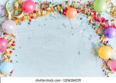 Carnival, festival or birthday balloon background with colorful party streamers, candy and confetti making a border on a blue background with copy space