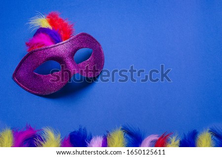 Carnival. Festive background with copy space. Violet carnival mask with feathers on a blue background. Mardi Gras. Brazilian. Venetian.
