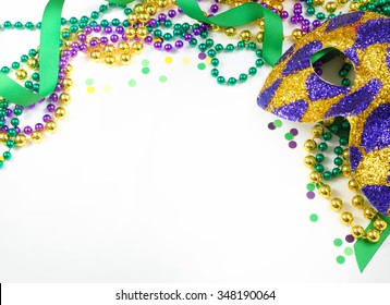 Carnival and Mardi Gras items including harlequin mask, green, gold and purple beads and ribbons and confetti on a warm white background. Copy space for your message. Horizontal composition