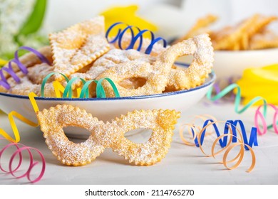 Carnival mask shape Angel wings or sfrappole or chiacchiere. Traditional sweet crisp pastry deep-fried and sprinkled with powdered sugar. Italian carnival food tradition. Paper serpentine.  - Shutterstock ID 2114765270