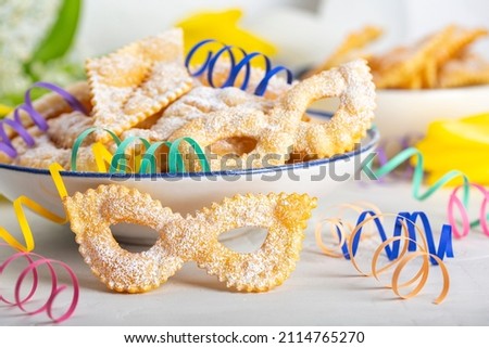 Carnival mask shape Angel wings or sfrappole or chiacchiere. Traditional sweet crisp pastry deep-fried and sprinkled with powdered sugar. Italian carnival food tradition. Paper serpentine. 