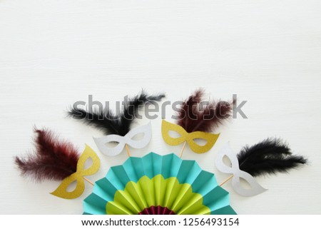 carnival party celebration concept with masks and colorful fan over white wooden background. Top view