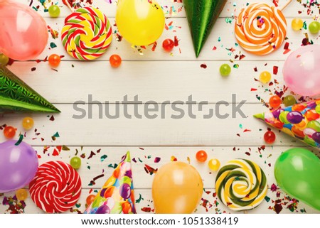 Carnival or party frame of colorful balloons, top view. Holiday decorations, lollipops and confetti on rustic wood planks with copy space for greeting, invitation or advertising. Birthday background