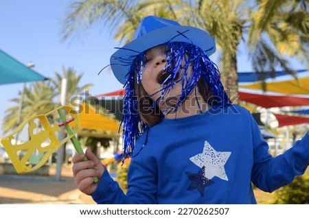Carnival, Purim in Israel. A cheerful little boy in a hat, funny glasses, a wig with a rattle, Raashan. Portrait of a child in a costume of Klana, a funny holiday, a birthday, a masquerade.
