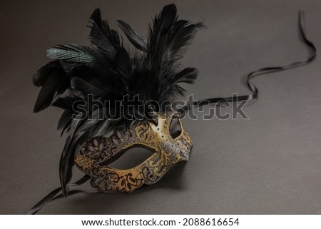 Carnival Venetian golden mask with black feathers on dark grey color background, copy space, template. Mardi Gras event disguise, traditional festival masquerade. 
