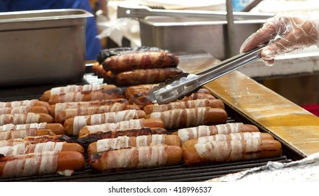 A Carnival Worker Grills Bacon Wrapped Hot Dogs.