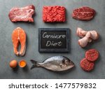 Carnivore diet concept. Raw ingredients for zero carb diet - meat, poultry, fish, seafood, eggs, beef bones for bone broth and words Carnivore Diet on gray stone background. Top view or flat lay.