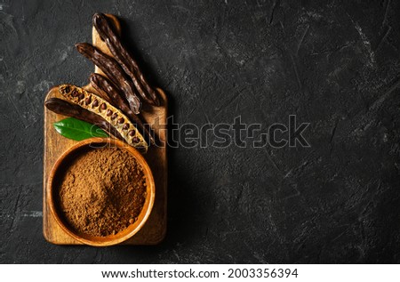 Carob bean and powder on board flat lay on black background, top view, copy space