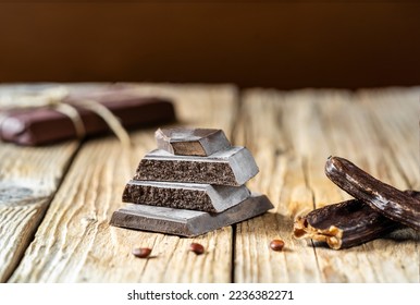 Carob chocolate, carob pods with seeds on rustic wooden background
