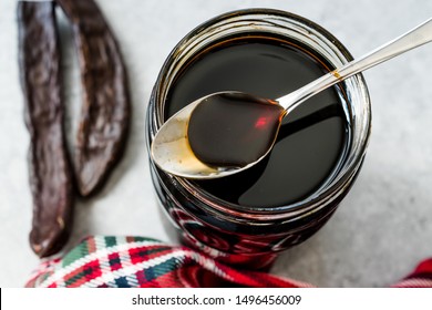 Carob Molasses Dripping From Spoon To Jar.