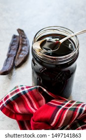 Carob Molasses Dripping From Spoon To Jar. Organic Food.