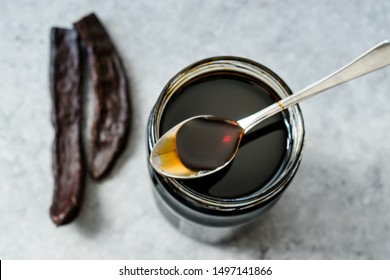 Carob Molasses Dripping From Spoon To Jar. Organic Food.