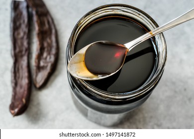 Carob Molasses Dripping From Spoon To Jar. Organic Food.