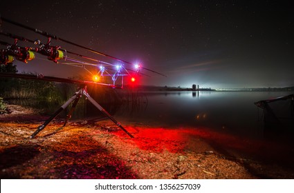 Carp Fishing Angling at lake at Night with illuminated Alarms. Night Fishing, Carp Rods, Close Up fishing Rods, Nightscape reflection on lake.