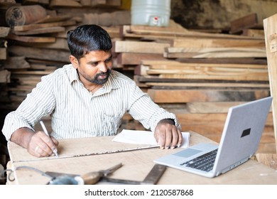 Carpainter Or Woodworker Measuring Wood By Seeing Blueprint Or Plan On Laptop At Workplace - Concept Of Technology, Artisan And Skilled Labour.