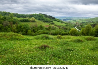 carpathian countryside landscape in spring. grassy meadows, rural fields and forested slopes on hills rolling off in to the distant village in the valley. overcast weather with clouds above the ridge