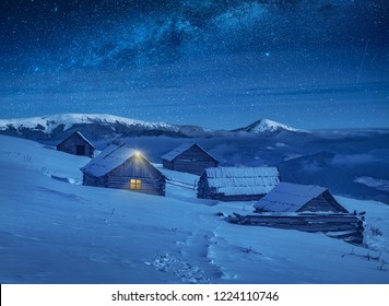 Carpathian Mountain Village Illuminated By Moon Light With Wooden Houses On A Hill Covered With Fresh Snow. Fantastic Milky Way In A Starry Sky. Christmas Winter Night.