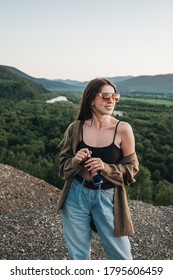 CARPATHIANS, UKRAINE - July 14, 2020: Beautiful Young Woman Enjoying Drinking Red Bull While Standing On Hill Over Beautiful Landscape, Female On Road Trip Having Energy Drink