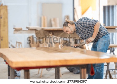 Carpenter applying protective varnish coating to a custom-made wooden table top