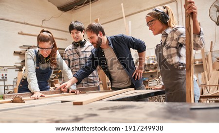 Carpenter apprentices with trainers at the circular saw in the carpentry workshop