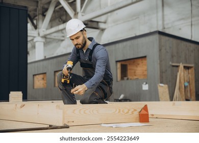 Carpenter assembling prefabricated house section using cordless screwdriver and screws in a modular building factory