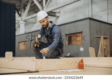 Carpenter assembling prefabricated house section using cordless screwdriver and screws in a modular building factory