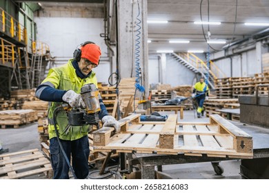 Carpenter assembling wooden pallets using a nail gun in a recycling factory, promoting sustainability and resource optimization