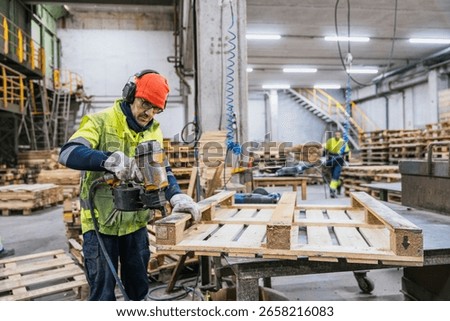 Carpenter assembling wooden pallets using a nail gun in a recycling factory, promoting sustainability and resource optimization