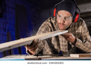 carpenter blowing sawdust from wooden plank after cutting with circular saw. man working in workshop - Powered by Shutterstock