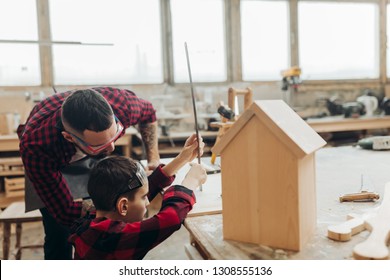 Carpenter Building A Wooden Birdhouse Together With His Kid. A Little Son Is Participating Actively In Hand Made Process. Happy Fatherhood And DIY Concept.