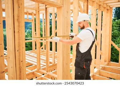 Carpenter building wooden frame house. Man measures the distance with tape measure while dressed in workwear and a helmet. - Powered by Shutterstock