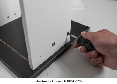 A carpenter builds a small white cabinet with a screwdriver