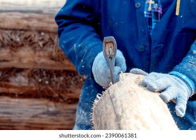 a carpenter builds a wooden house with an axe in his hand. High quality photo - Shutterstock ID 2390061381