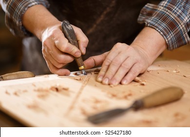 Carpenter With Chisel In The Hands On The Workbench