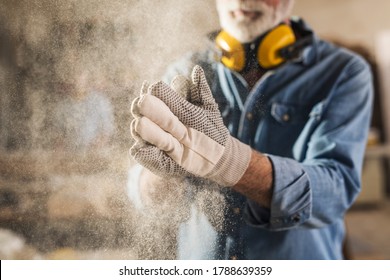 Carpenter cleaning work gloves from sawdust after he finished processing the wood