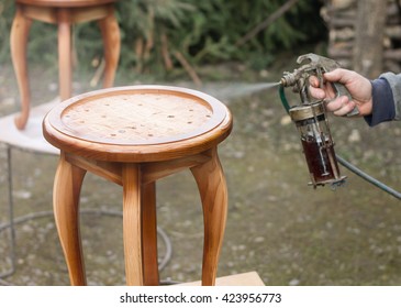 Carpenter Is Covering Stool By Lacquer. Furniture Varnishing Using Sprayer (pulverizer).