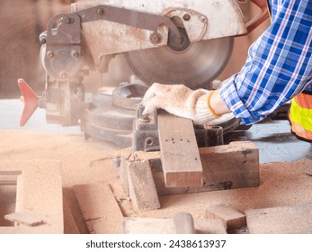 The carpenter craftsman wearing safety gear working with hardwood using a miter saw to cut a piece of wood in the workshop. Manufacture of wood products. - Powered by Shutterstock