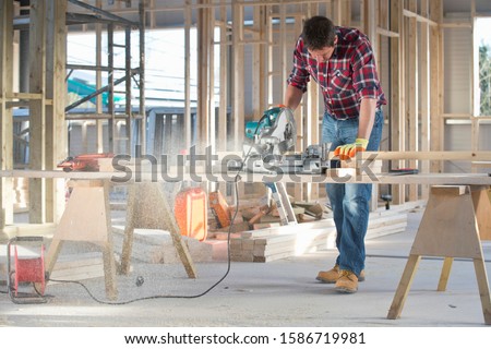 Carpenter cutting wood with circular power saw in building construction site interior