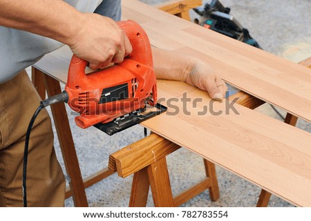 Carpenter cutting a wooden panel for wooden floor with the jigsaw, carpentry tools