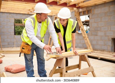 Carpenter With Female Apprentice Working On Building Site