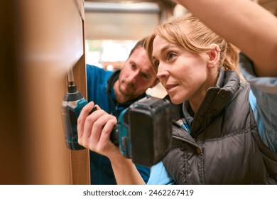 Carpenter With Female Apprentice In Workshop Using Drill To Attach Piece Of Wood To Window Frame - Powered by Shutterstock