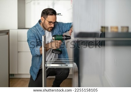 Carpenter finalizing the assembly of the kitchen.Man installing furniture and equipment in the kitchen, using electric screwdriver.Construction, maintenance and repair concept.