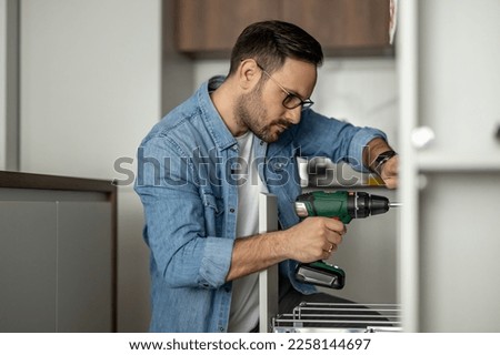 Carpenter finalizing the assembly of the kitchen.Man installing furniture and equipment in the kitchen, using electric screwdriver.Construction, maintenance and repair concept.