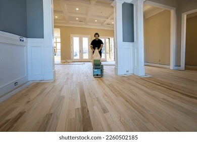 Carpenter grinding a wooden parquet floor by using floor sander in newly constructed house to ensure that it is smooth even - Shutterstock ID 2260502185