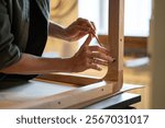 Carpenter hands use hex key to screw bolts, attaching table legs to wooden tabletop in workshop. Furniture assembly, sturdy construction, woodwork production, custom design, manual labor, tool mastery