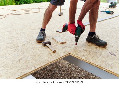 Carpenter holds a carpentry tool. Roofer with drill installing wooden panels. Worker working on the roof at construction site. Preparation for carport construction. 