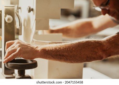 Carpenter or joiner working on a wooden cabinet on a workbench adjusting a wheel on a machine with his hand as he guides the unfinished product in a close up view