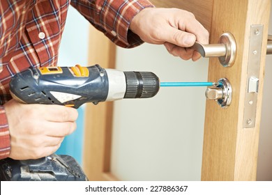 carpenter at lock installation with electric drill into interior wood door