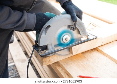 Carpenter man using circular saw to cut timber, close up work process. Frame house construction, DIY eco wooden home concept. Skilled worker cutting  wood plank with electric tool outdoor.
