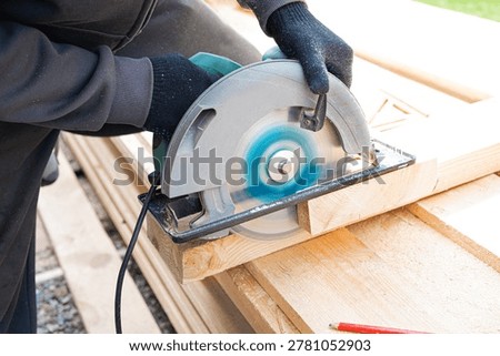 Carpenter man using circular saw to cut timber, close up work process. Frame house construction, DIY eco wooden home concept. Skilled worker cutting  wood plank with electric tool outdoor.